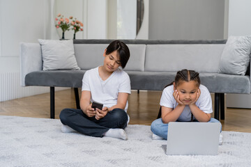 Asian girl watching film on laptop while brother using smartphone at home
