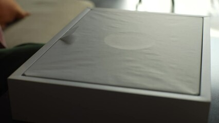 Ufa, Russia - 10 October 2022. Close-up hands of unrecognizable happy young man unpacking latest cardboard box Apple MacBook Pro 16 inch sitting on sofa at desk in sunny living room. Online shopping