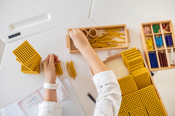 Male kid hands counting math with golden bank Montessori material beads block desk closeup top view