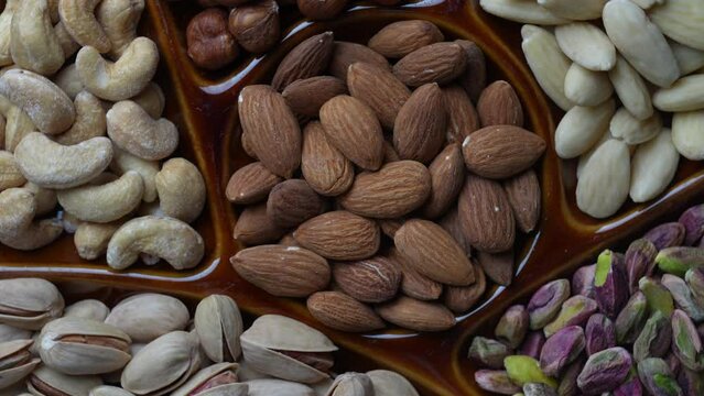 Assortment of nuts in ceramic bowl on a wooden background, close up, top view, rotate. Cashew, hazelnuts, pistachios and almonds nuts for eat. Vegetarian meal. Healthy eating concept