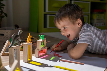 Male kid playing wooden bricks and dinosaurs drawing shadow on paper early development education