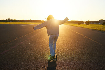 Teen girl feeling happy on longboard. Happy young skater riding her skateboard with hands spread...