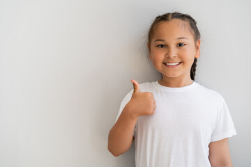 Smiling asian girl showing like gesture and looking at camera at home