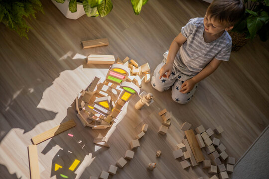 Cute baby boy building tower wooden bricks Montessori materials at sunny home room interior