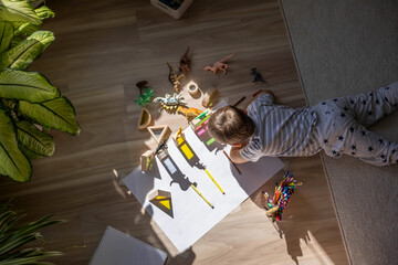 Male kid playing wooden bricks and dinosaurs drawing shadow on paper early development education
