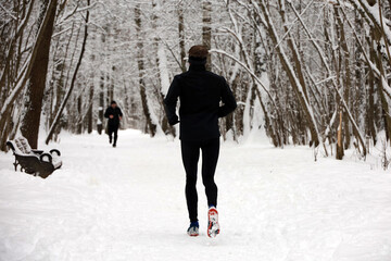 Man in black sportswear running in winter park by the snow. Workout on nature, runners in cold season - Powered by Adobe