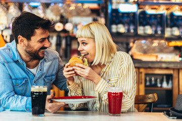Young couple in love having fun spending leisure time together at restaurant, eating burgers and drinking beer