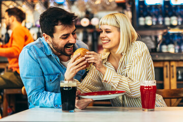 Young couple in love having fun spending leisure time together at restaurant, eating burgers and drinking beer