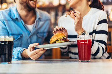 Young couple in love having fun spending leisure time together at restaurant, eating burgers and...