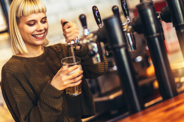 Female bartender tapping beer in bar.
