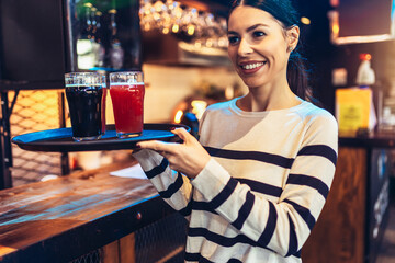 Young female waitress or bartender serving drinks in a bar carrying a tray with beer