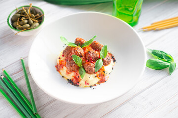 Beef meatballs in tomato sauce with mashed potatoes and basil in a white plate on a wooden background