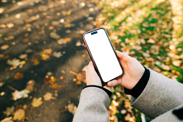 Man holding smartphone with a white screen mock up while walking on a park.