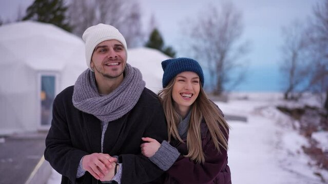 Dolly shot portrait of satisfied young couple walking arm in arm talking looking away. Medium shot of happy confident loving Caucasian man and woman strolling on winter day outdoors