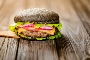 Side view of black burger with artificial meat and fresh greenery on wooden table. Selective focus