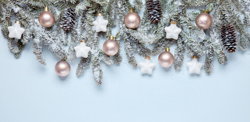 Christmas bbanner with fir branches and decorations in pastel colors, with snow. Elegant Christmas banner from fir branches, beige balls and white stars, in muted colors on a light blue background