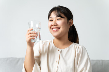 healthy beautiful young woman holding a glass of water sitting on the couch at the livingroom.