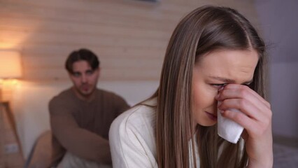 Close-up portrait of depressed offended woman crying sitting on the right with blurred man yelling at background. Frustrated Caucasian beautiful girlfriend arguing with unfaithful boyfriend