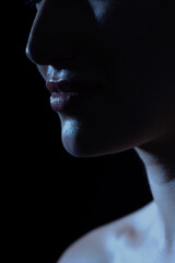 Fashion, beauty and make-up concept. Close-up dark face silhouette of beautiful and sexy woman. Part of model face covered in shadow. Sensual mood. Lips in camera focus. Toned image with blue color