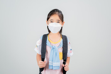 Asian little child girl carry a backpack wearing respirator mask to protect coronavirus outbreak and pointing hand to blank background, New virus Covid-19