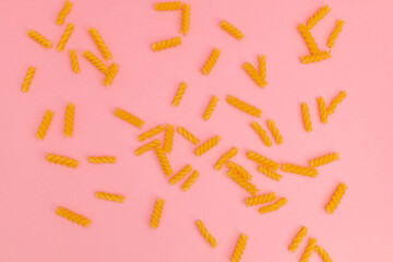 Raw macaroni scattered on pink background