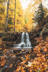 Wonderful cascading waterfall Bystry covered and surrounded by autumn leaves and trees glowing orange-red at the village Čeladná in the heart of Beskydy mountains, Czech republic
