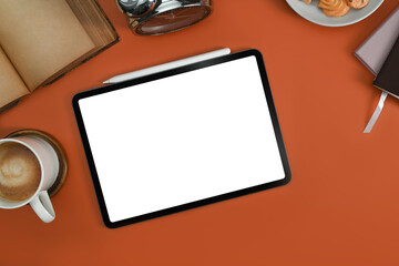 Flat lay digital tablet with white screen, coffee cup and book on orange background
