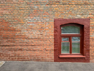 An empty wall of an old brick house, a window and a lawn. Red brickwork in a historic industrial building.