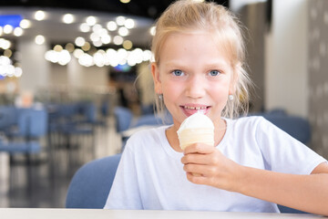 Portrait of a little hungry funny girl eating cold delicious ice cream in a waffle cup sitting in a cafe, dark background, bokeh. A child enjoys ice cream. A sweet snack