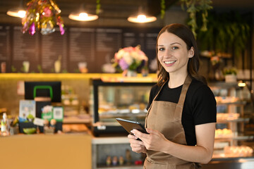 Portrait of cafe owner smiling cheerfully using a digital tablet in front of the counter in modern coffee chop
