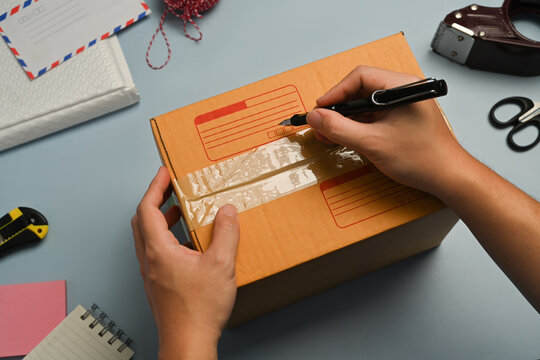 Cropped image of man writing address on carton box, seller preparing parcel box of product for shipping