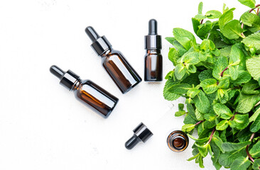 Obraz premium Essential oil of mint or peppermint in small brown bottles with fresh green plant, white background, top view