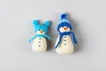 Two funny knitted snowmen in blue hats and scarves on a gray background. Merry Christmas and New Year 2023 greeting card