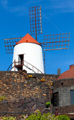 View of windmill at Jardin de Cactus, botanical cactus garden in Guatiza, on Lanzarote island. Sightseeing with volcanic rocks, green wild plants, blue sky and no people. Canary islands, Spain.