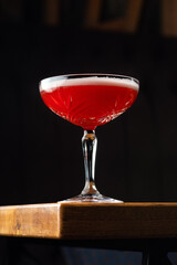 Red Cocktail in Coupe Glass with Layer of Foam on black Background