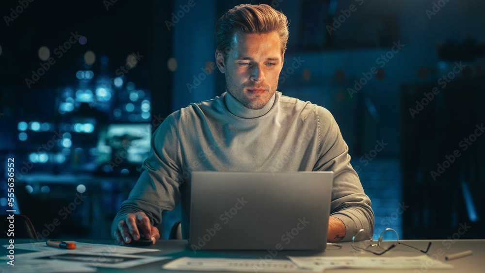 Poster portrait of a stylish male working on laptop computer in a company office in the evening. young mana