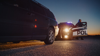 Black Female Police Officer Stepping Out of Patrol Car and Heading Towards a Pulled over Car. Cops Responding to a 911 Call About a Suspicious Car Stopped on the Road, Investigating the Situation © Gorodenkoff