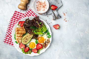 Fototapeta na wymiar Plate with keto diet food. Keto breakfast Fried egg, avocado, strawberry, grilled chicken fillet, nuts and fresh salad, Ketogenic diet. Healthy food concept, top view