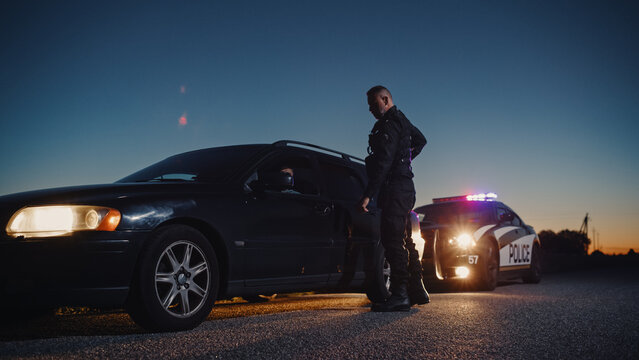 Portrait of Middle Aged Caucasian Cop Approaching a Pulled Over Car with Caution. Drunk Driver Being Stopped by an Officer to Inspect his Papers. Police Officer Keeping the Road Safe