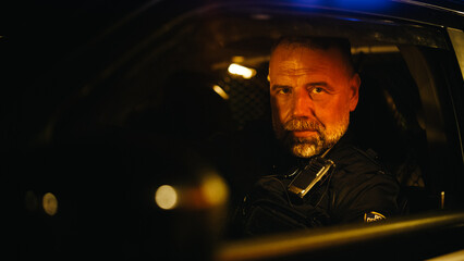 Portrait of Police Officer Sitting in the Patrol Car, Looking at the Camera. Officer of the Law...