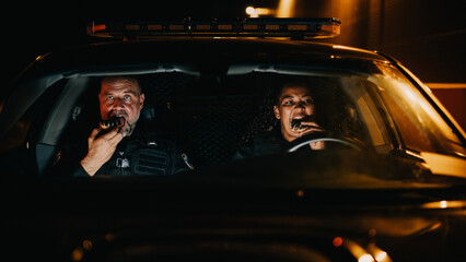 Two Police Officers Sitting in Traffic Patrol Car, Eating Donuts. Police Partners Enjoying their...