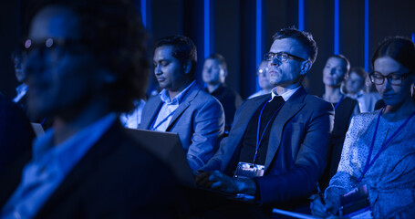 Young Man Sitting in a Crowded Audience at a Business Conference. Corporate Delegate Watching...