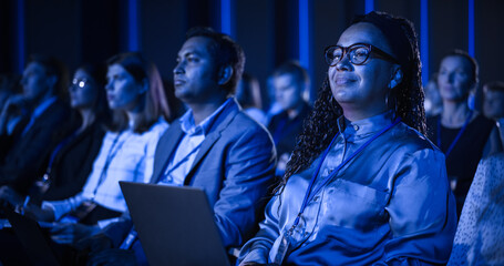 Black Female Sitting in Dark Crowded Auditorium at an International Business Conference....