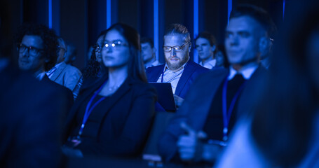 Young Bearded Man Attending an IT Conference in Crowded Audience. Delegate Using Laptop Computer....