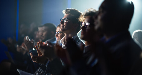 Young Man Sitting in a Crowded Audience at a Business Conference. Male Attendee Cheering and Clapping After a Motivational Keynote Speech. Auditorium with Young Successful Businesspeople. - obrazy, fototapety, plakaty