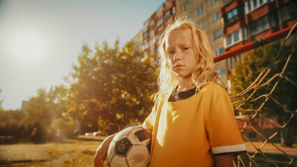 Portrait of a Beautiful Blond Girl in Yellow T-Shirt Holding a Soccer Ball, Standing Next to a Goal Gate in a Backyard. Young Football Player Looking at Camera, Being Focused. Cold Color Grading.