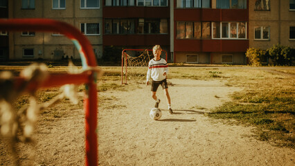 Young Handsome Boy Practising Dribbling with Soccer Ball and Shooting Penalty Kicks. Talented Football Player Practicing Free Kicks in the Backyard, Dreaming to Go Professional