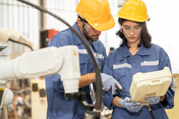 Female industrial engineer using remote control board to check robotic welder operation in modern automation factory. Technician man monitoring robot controller system for automated steel welding. © Nassorn