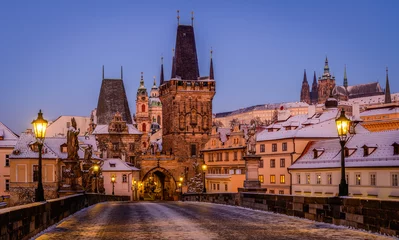 Poster Charles Bridge covered in snow with shining lanterns in Prague during blue hour in the winter morning. © Ondrej Bucek
