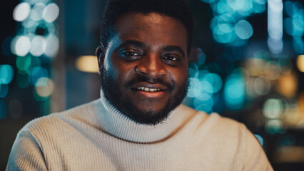 Close Up Portrait of a Handsome Black Man Wearing Stylish White Turtleneck, Looking at Camera and Expressing a Perfect Smile. Happy Attractive Manager at Work in Office in the Evening.